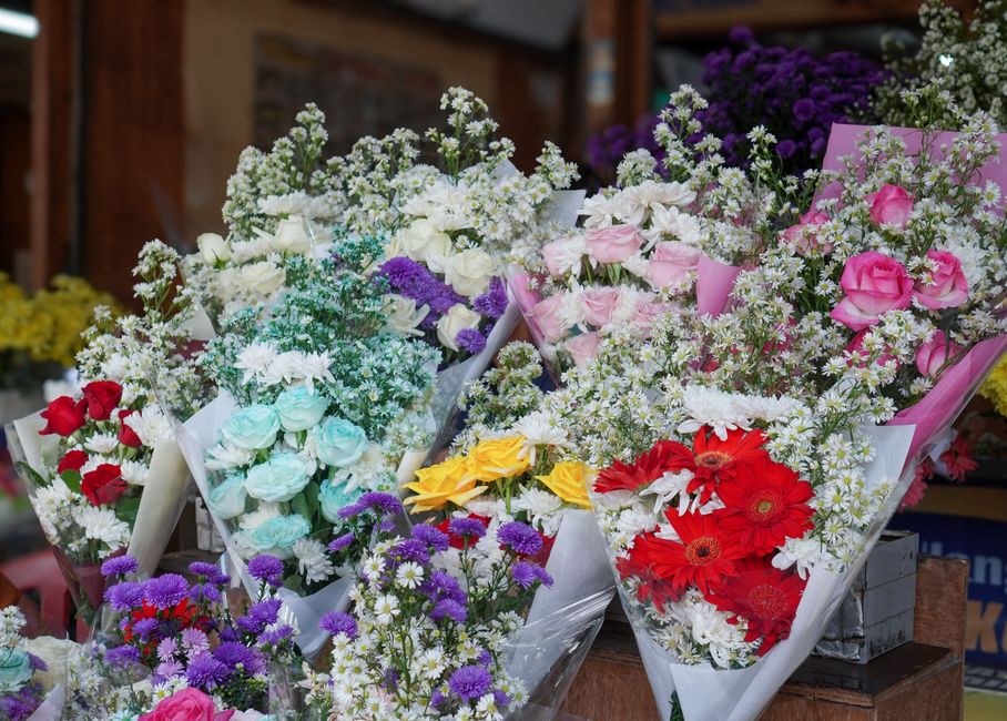 An assortment of fresh flower bouquets displayed on a wooden surface, featuring a variety of flower types and colors. One bouquet includes pink roses with white baby's breath wrapped in soft pink pape